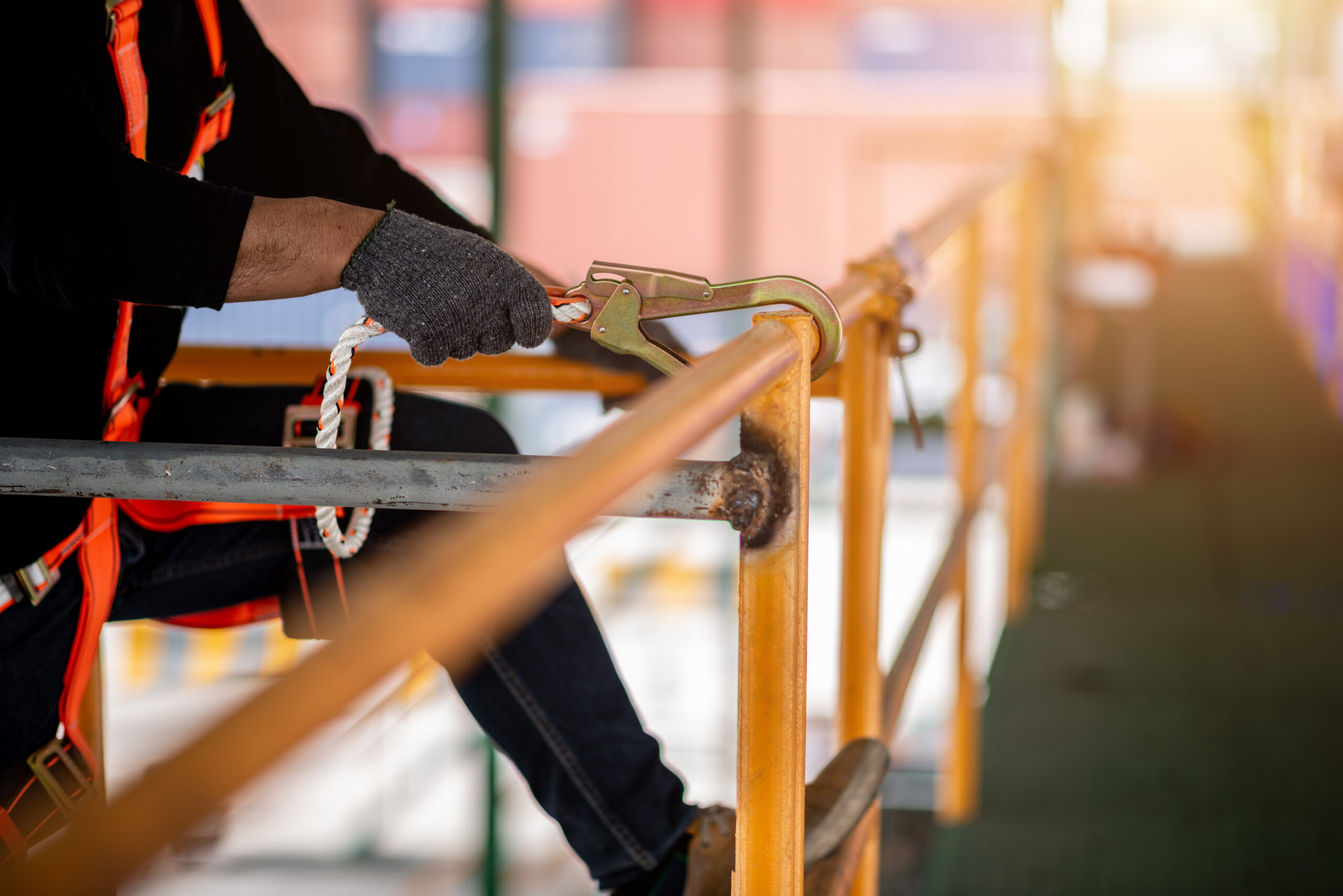 Construction worker securing height safety harness on scaffolding and guardrail.