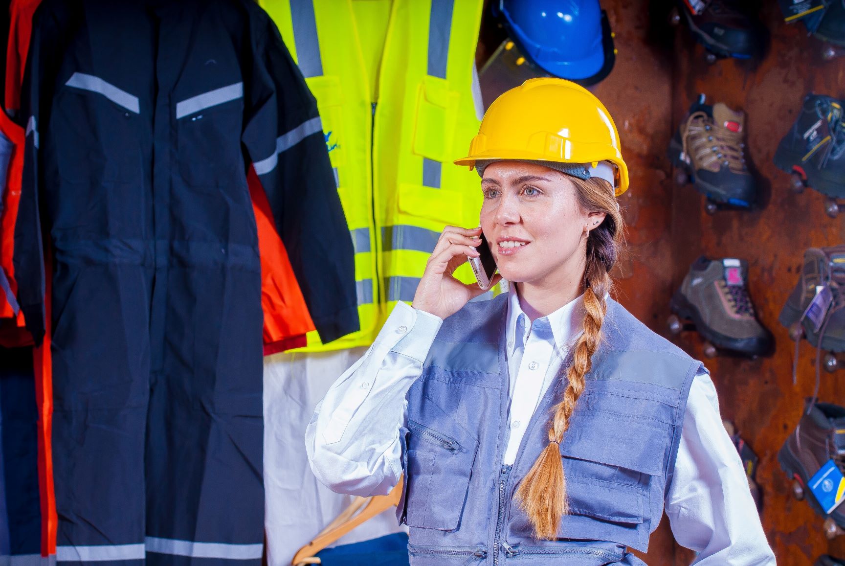 Woman wearing high-visibility clothing and hard hat talking on mobile phone, demonstrating workplace safety during the holiday season.
