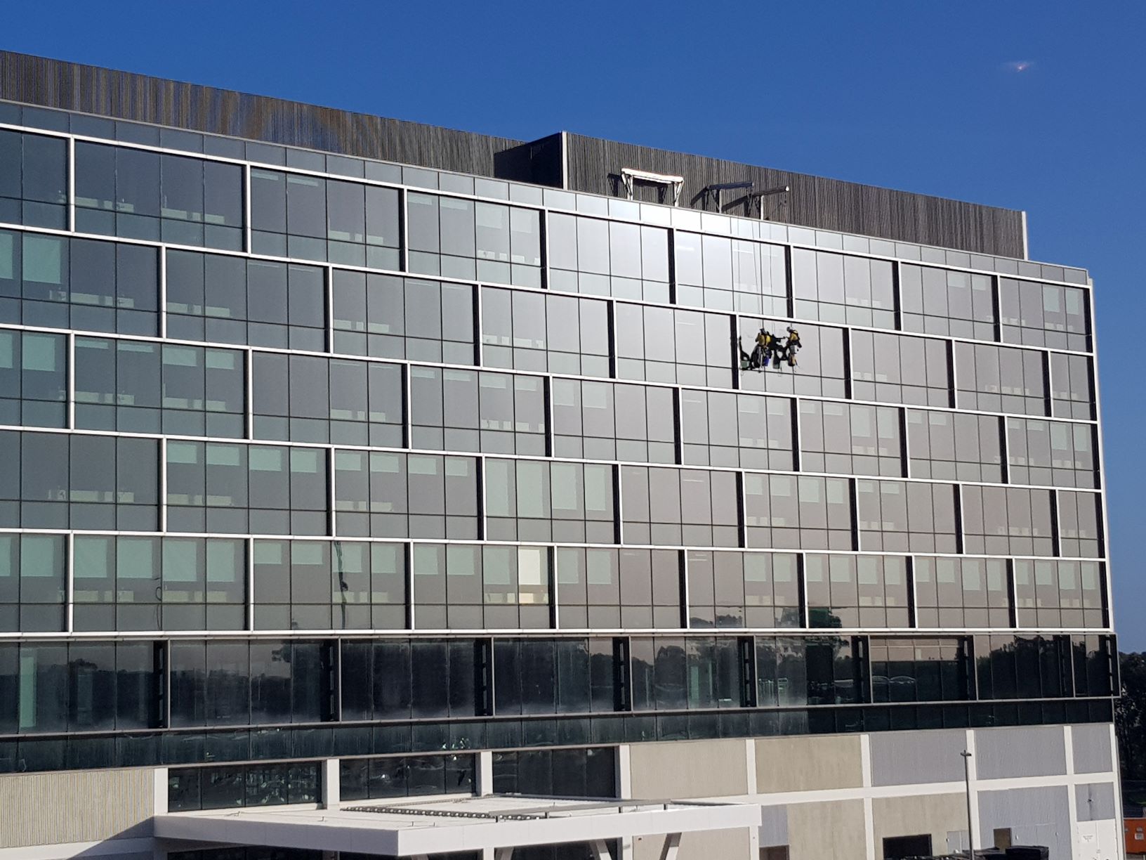 Davit arm façade access system attached to building and workers performing maintenance
