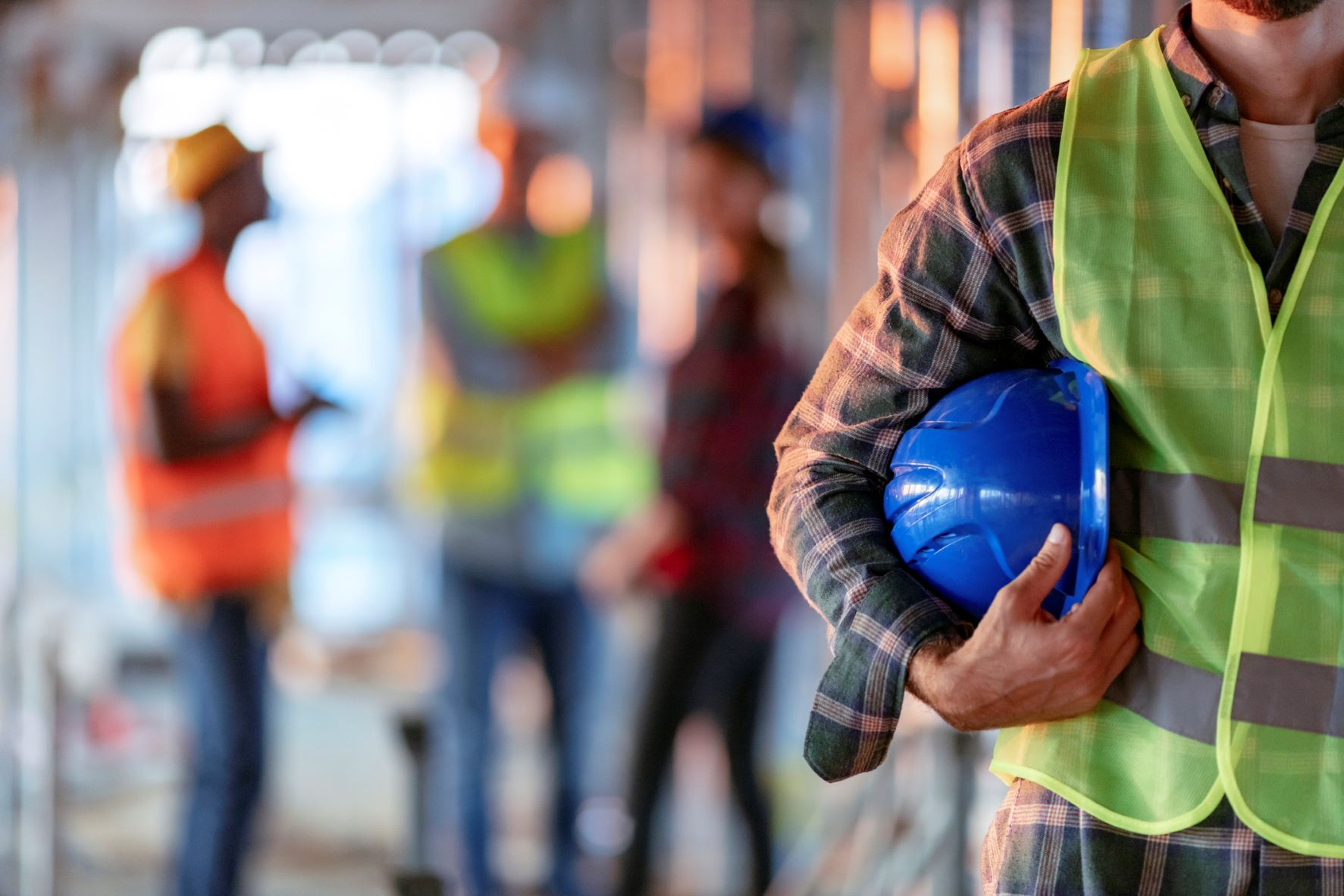 Construction worker holding a blue safety helmet and wearing a high-visibility vest, illustrating a safe workplace.