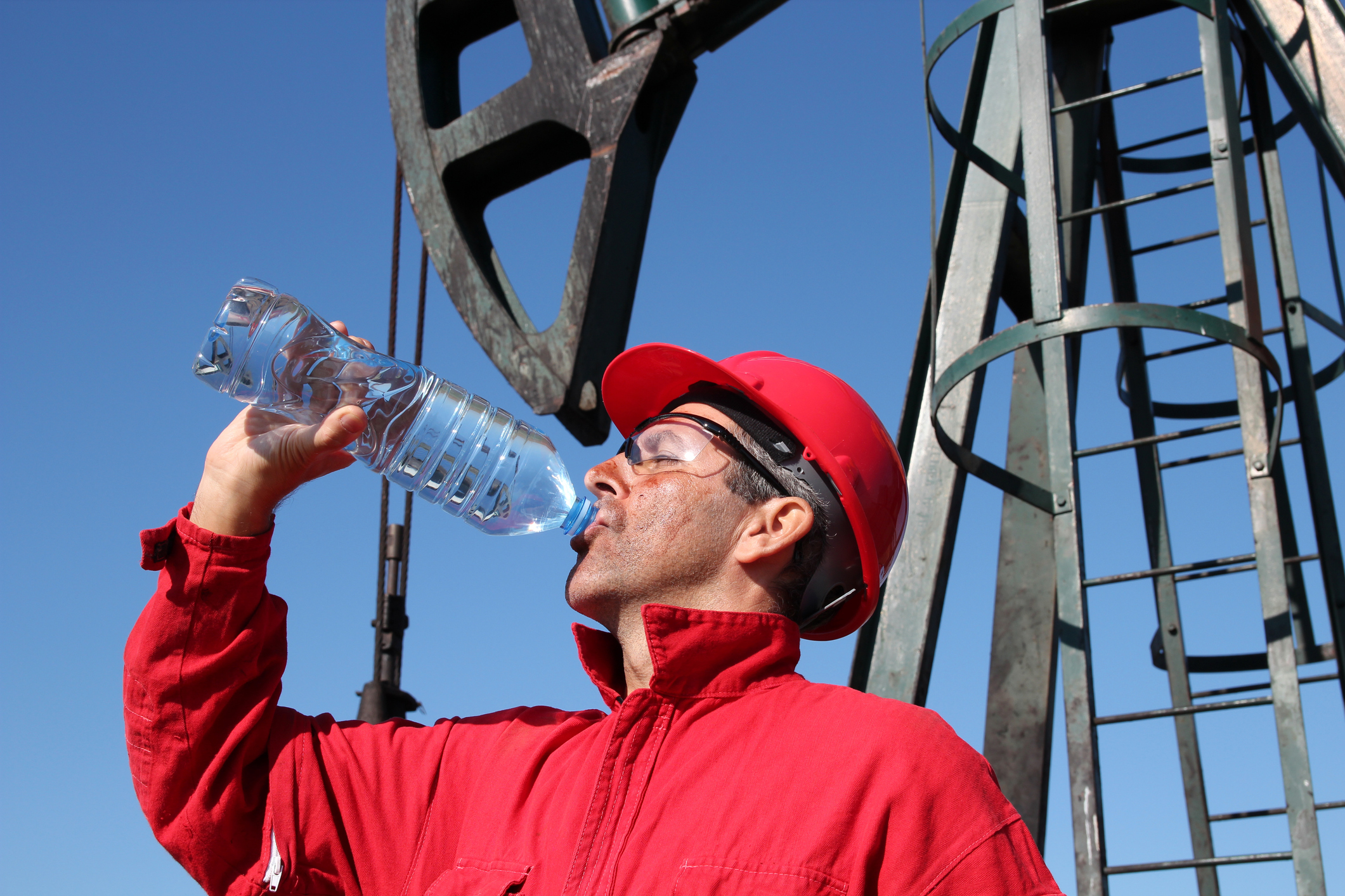 Construction worker drinking water under hot sun, outdoor work safety and hydration.