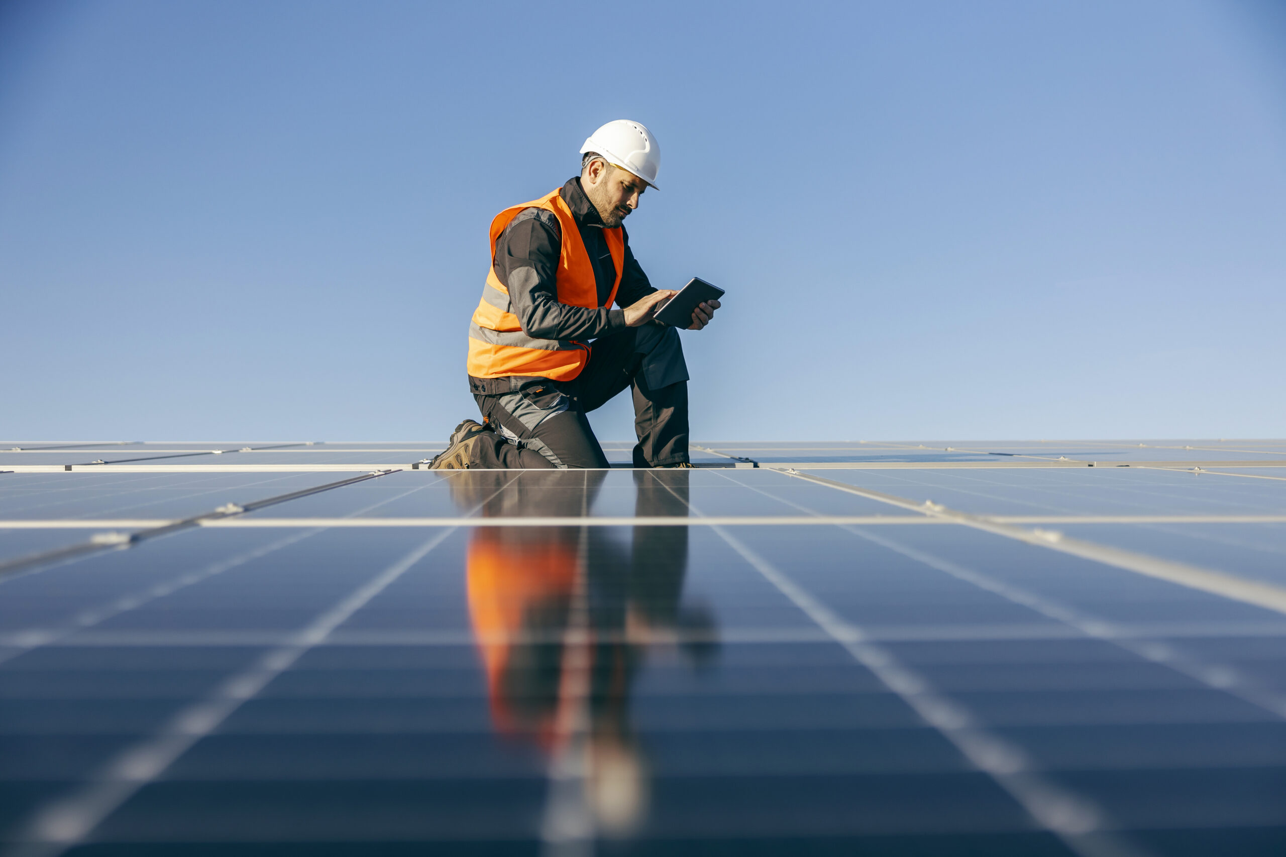 Solar panel installer reviewing tablet on rooftop, demonstrating fall risk management and compliance.