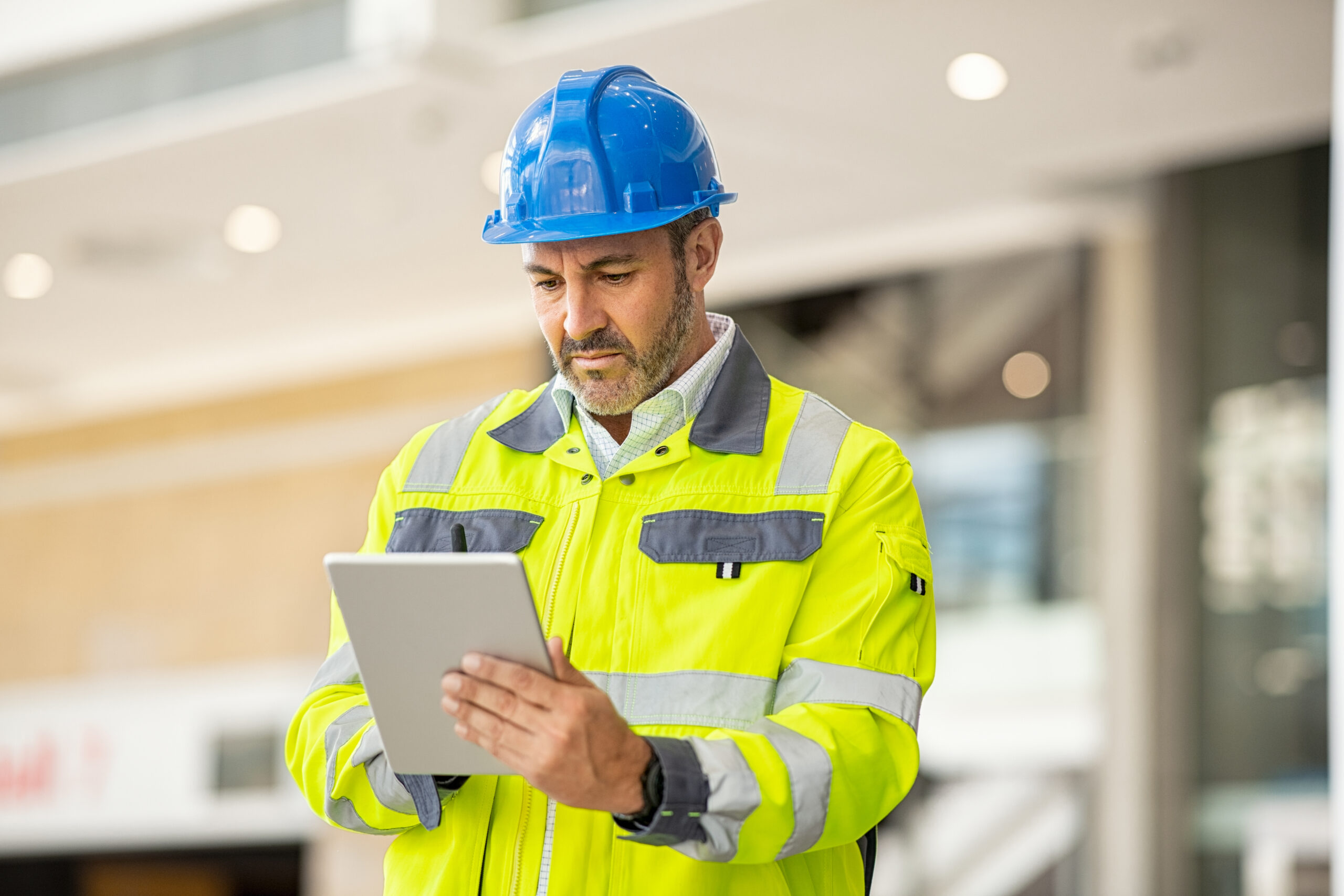 Construction worker wearing a hard hat and high-visibility vest reviewing tablet for workplace safety improvements and NSW rebate program.