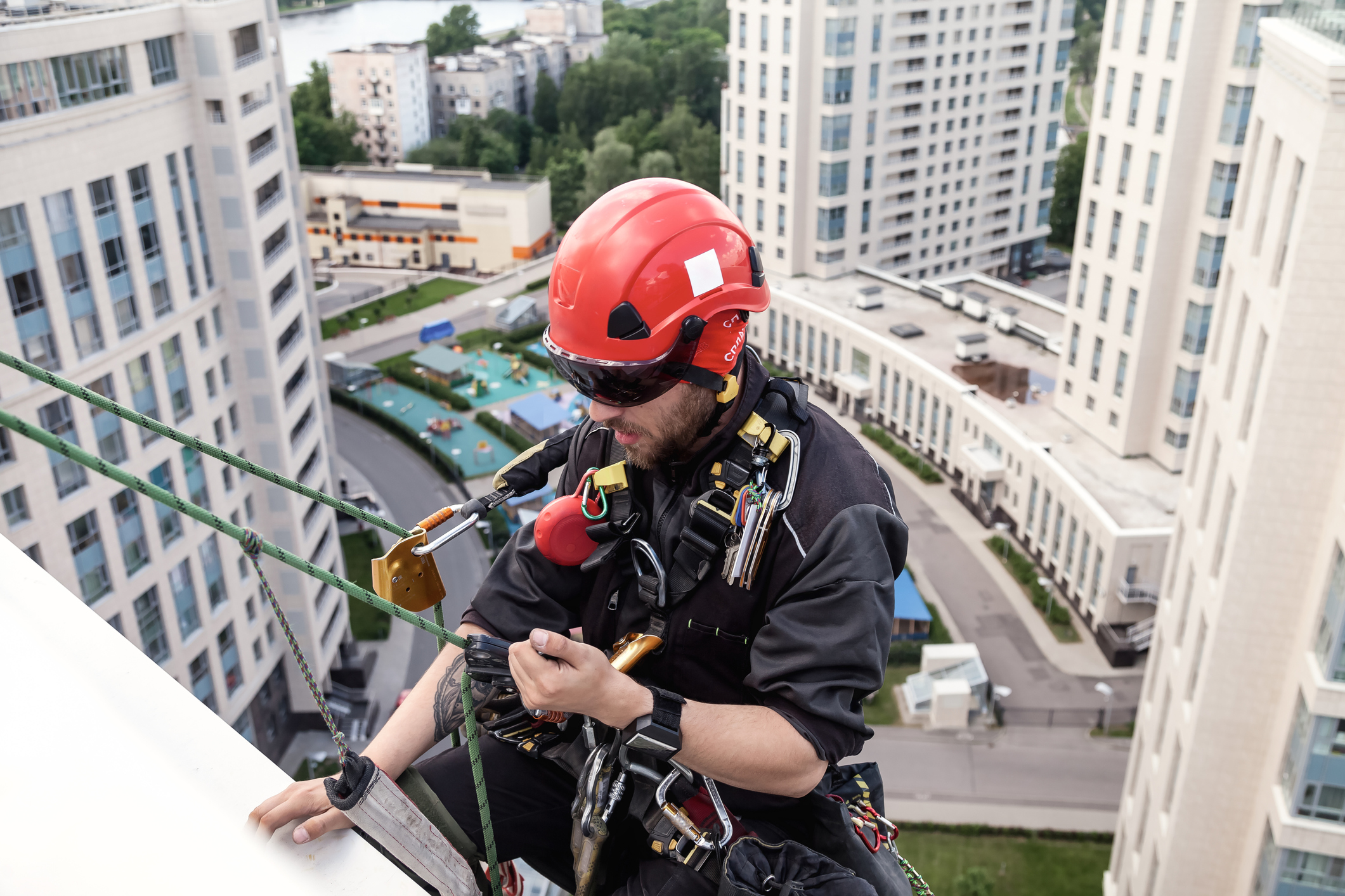 Worker wearing height safety equipment and harness on building roof for recertification inspection.