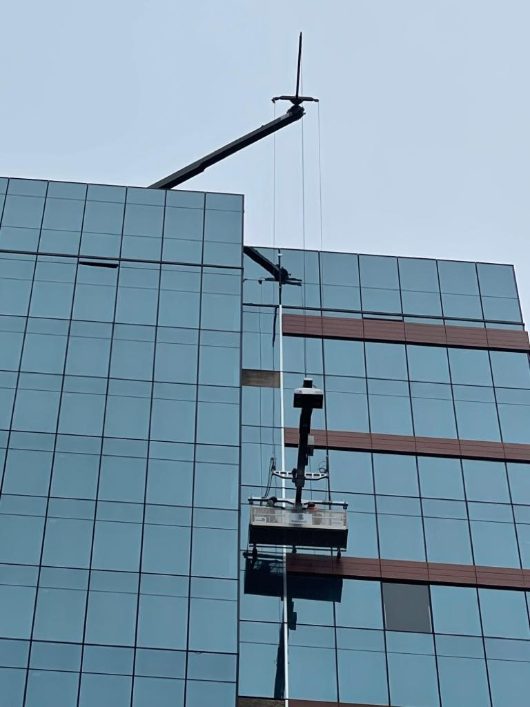 High-rise building facade with a suspended platform and crane for safe access and maintenance, illustrating RISSafety's commitment to roof safety systems.