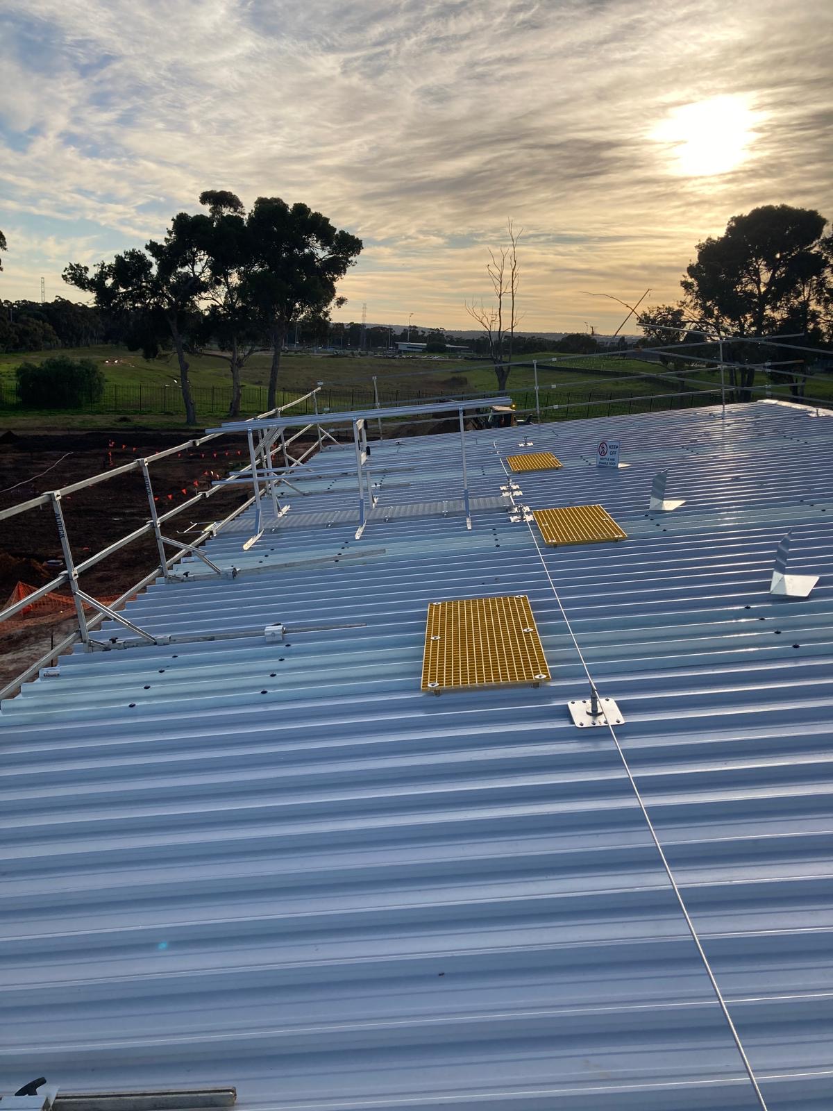 Roof access system installation with safety rails and yellow safety mats, overlooking a construction site at sunset, highlighting RISSafety's height safety solutions.